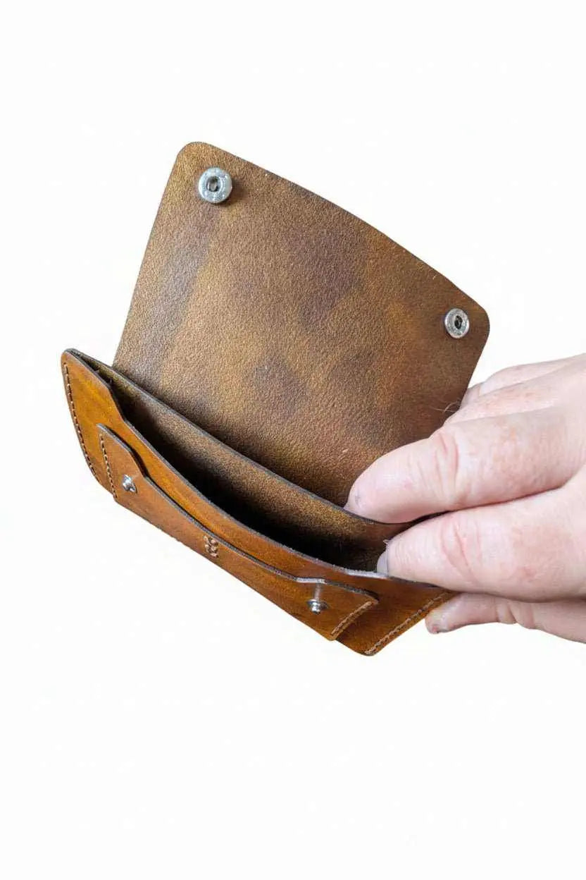 Handmade brown leather wallet being held open to show interior pockets and metal rivets.